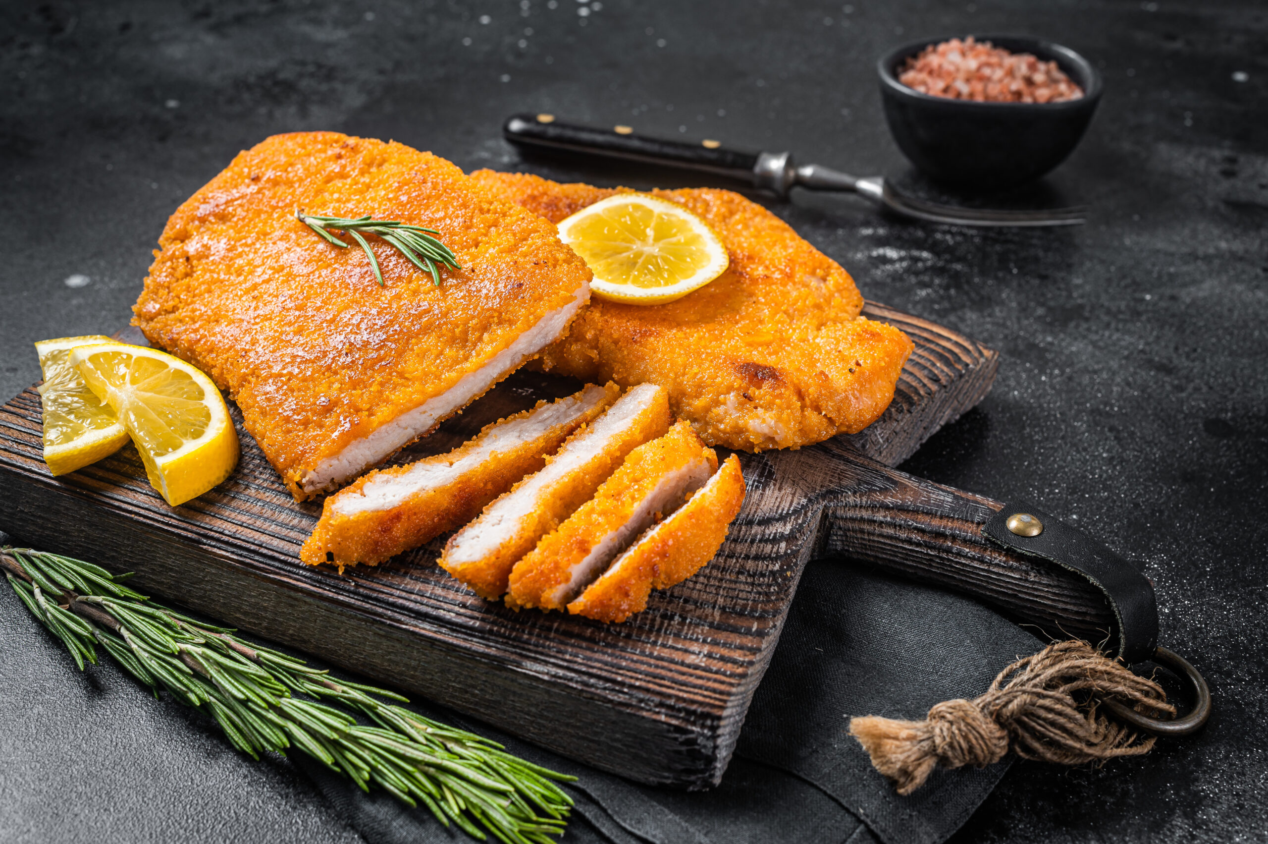 Fried sliced weiner schnitzel on a wooden board with herbs. Black background. Top view.