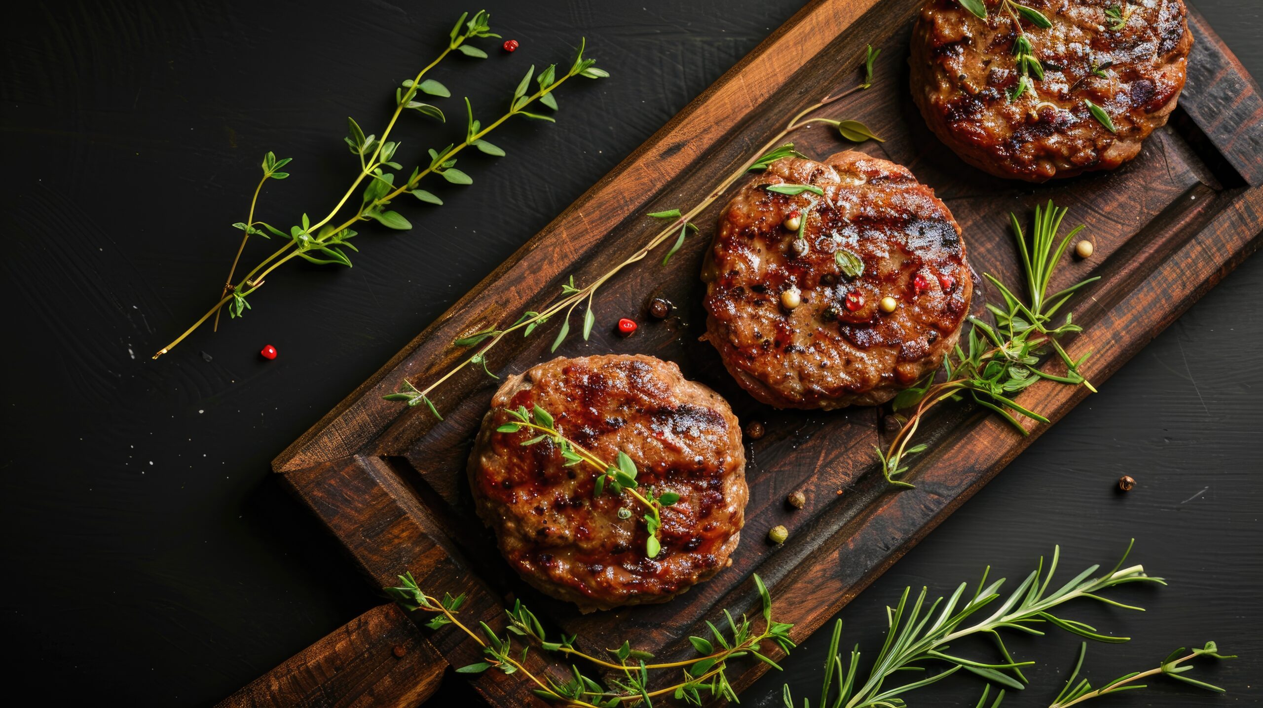 BBQ beef meat burgers on wooden board with herbs black background top view